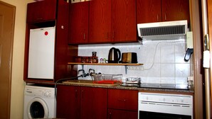 A compact kitchen with wooden cabinets, a washing machine, a dishwasher, and a coffee maker on the countertop. - Happy Home 4 (Limassol)