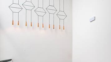 Un interior moderno con suelo de madera, un tapete estampado, una silla negra, una mesita pequeña y una lámpara de techo con un diseño geométrico único.