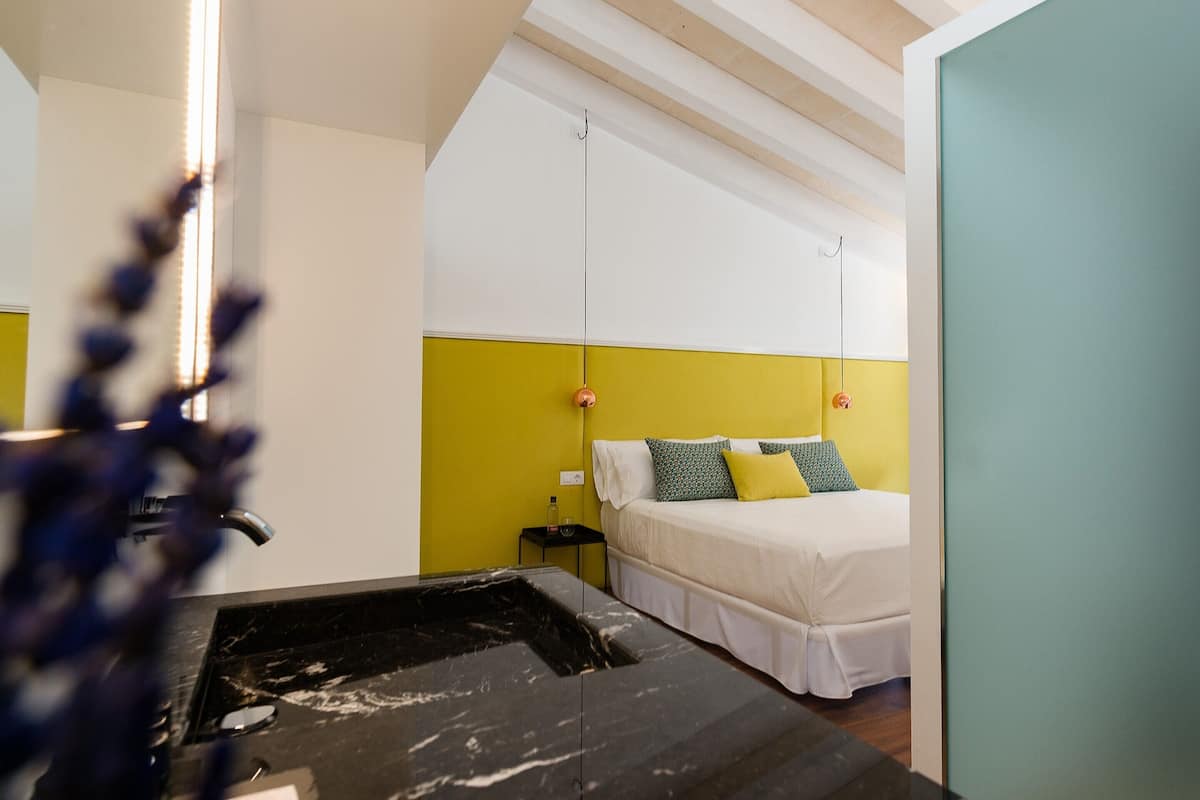 Une chambre d’hôtel comprenant un lit, une table de chevet et une salle de bain avec un lavabo et un miroir.