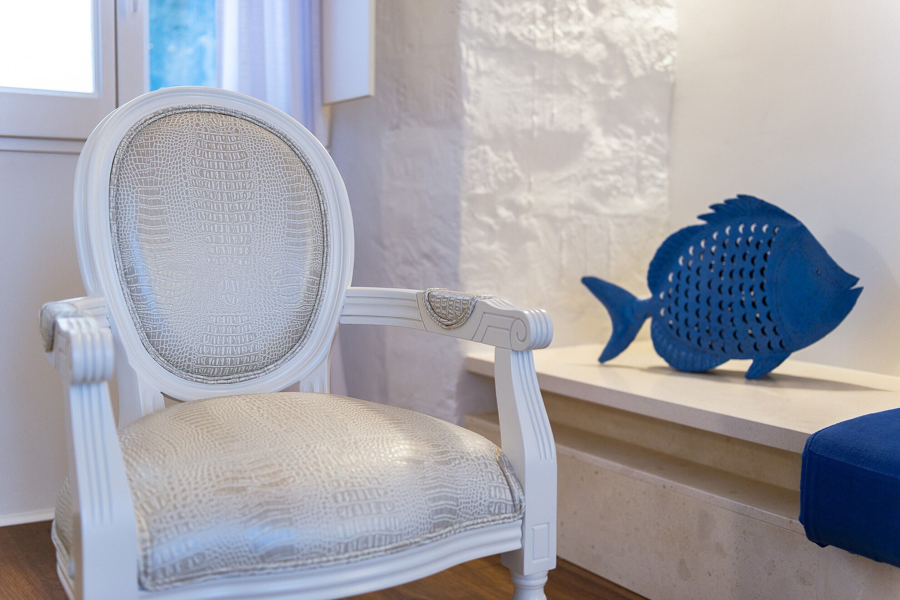 Una silla blanca con asiento y respaldo texturizados, ubicada cerca de una ventana con vistas al exterior.
