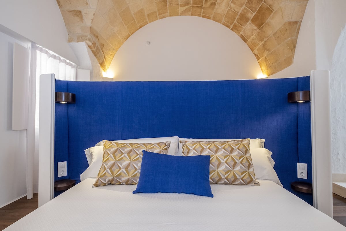 Une chambre à coucher avec un lit blanc, une tête de lit bleue et des coussins à motifs.
