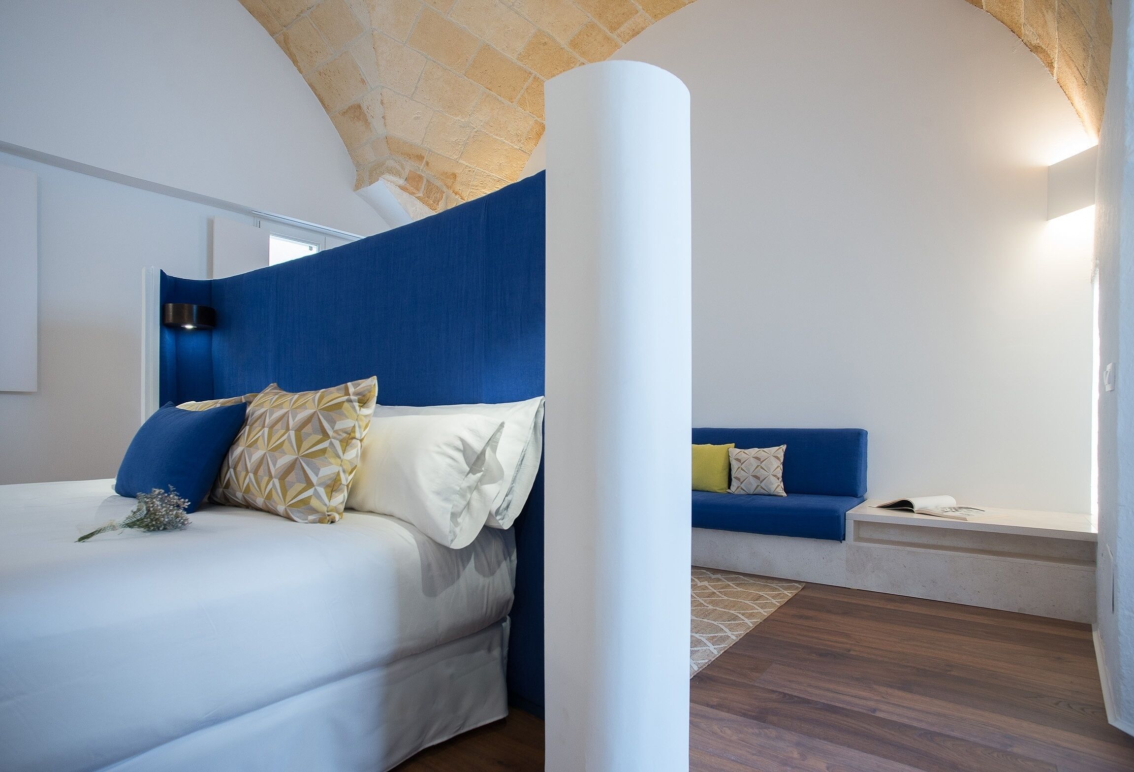 A bedroom with a bed, a blue sofa, a white pillar, and a stone ceiling.