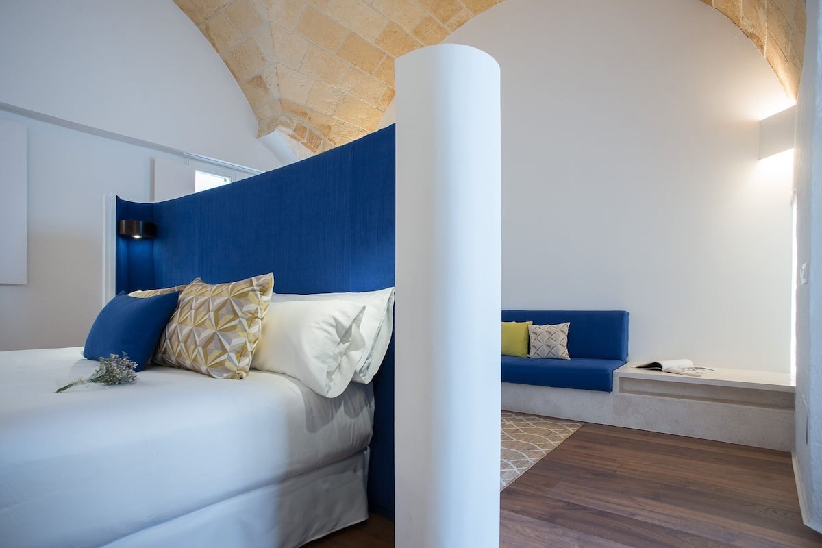 Une chambre à coucher avec un lit, un canapé bleu, un pilier blanc et un plafond en pierre.