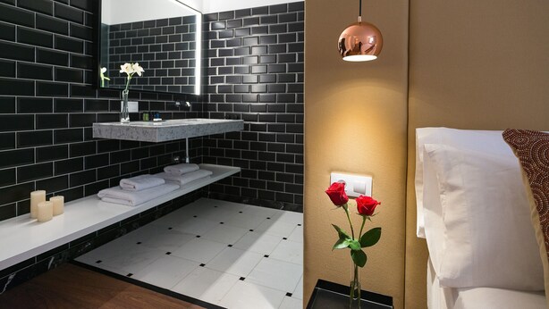 A modern bathroom with a black brick wall, a white sink, and a wooden floor.
