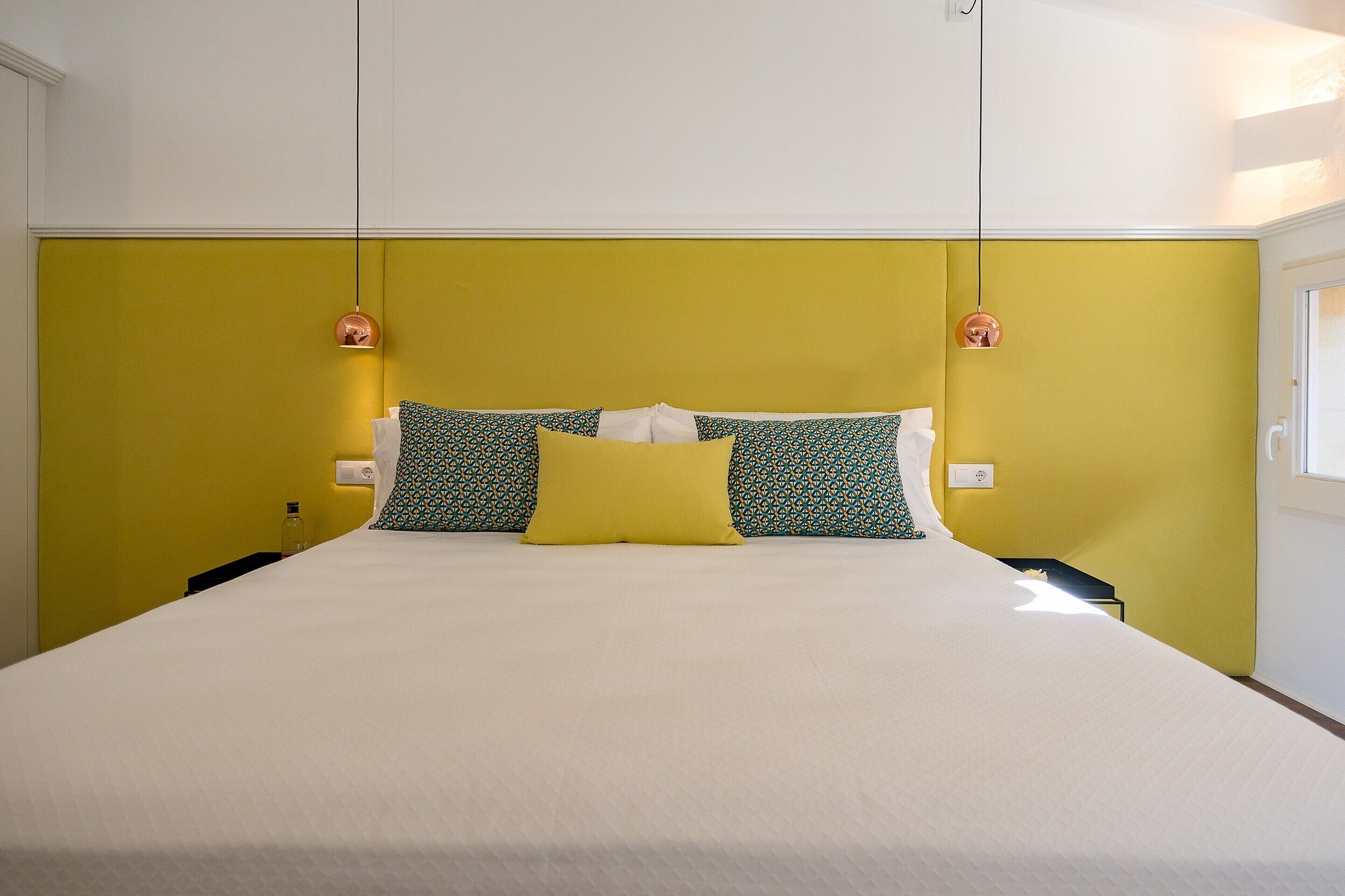 A bed with white bedding, a yellow headboard, and patterned pillows.