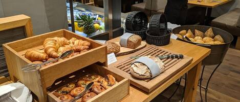 Un bufé de desayuno con diversas pastas y pan exhibido sobre mesas de madera.