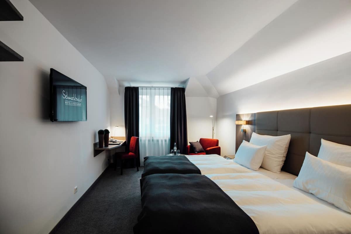 Una habitación de hotel con una cama grande, un escritorio con silla, un televisor montado en la pared y una ventana con cortinas.