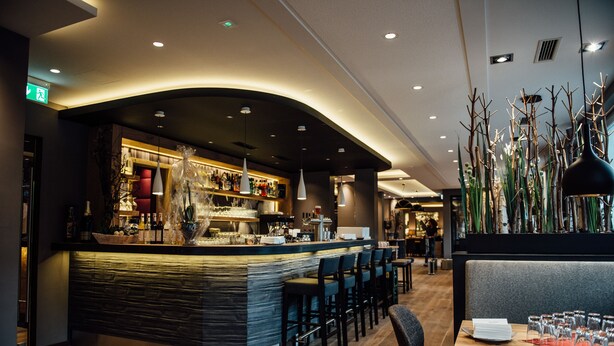 Un espace bar moderne doté d’un comptoir incurvé, de sièges et de plantes décoratives.