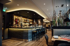 Un espace bar moderne doté d’un comptoir incurvé, de sièges et de plantes décoratives.