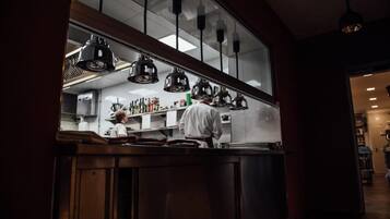 A kitchen area with a chef preparing food, a counter with various kitchen items, and hanging pendant lights.