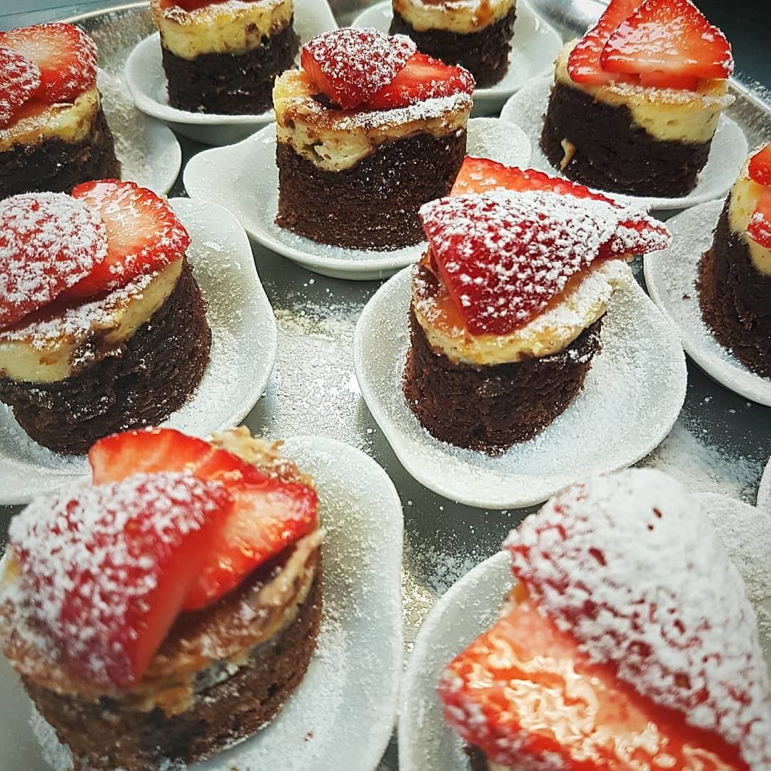 A display of desserts, each topped with strawberries and powdered sugar.