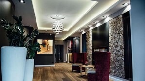 Un hall d’entrée moderne avec un plancher en bois, une grande plante en pot, un lustre et des fauteuils à revêtement rouge.