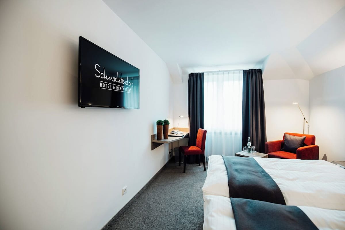 Habitación de hotel con cama, escritorio con silla, televisor en la pared y ventana con cortinas.