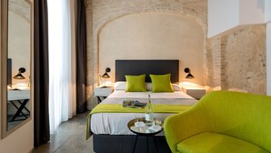 Camera d'albergo con un letto grande, cuscini verdi, un comodino con una lampada e una poltrona verde brillante.