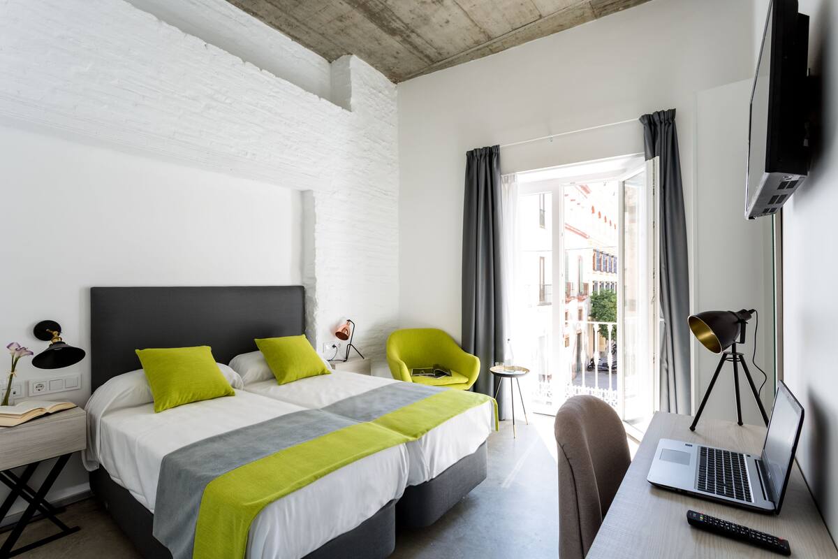 Een moderne hotelkamer met een groot bed, een bureau met een laptop, een stoel en een aan de muur bevestigde televisie.