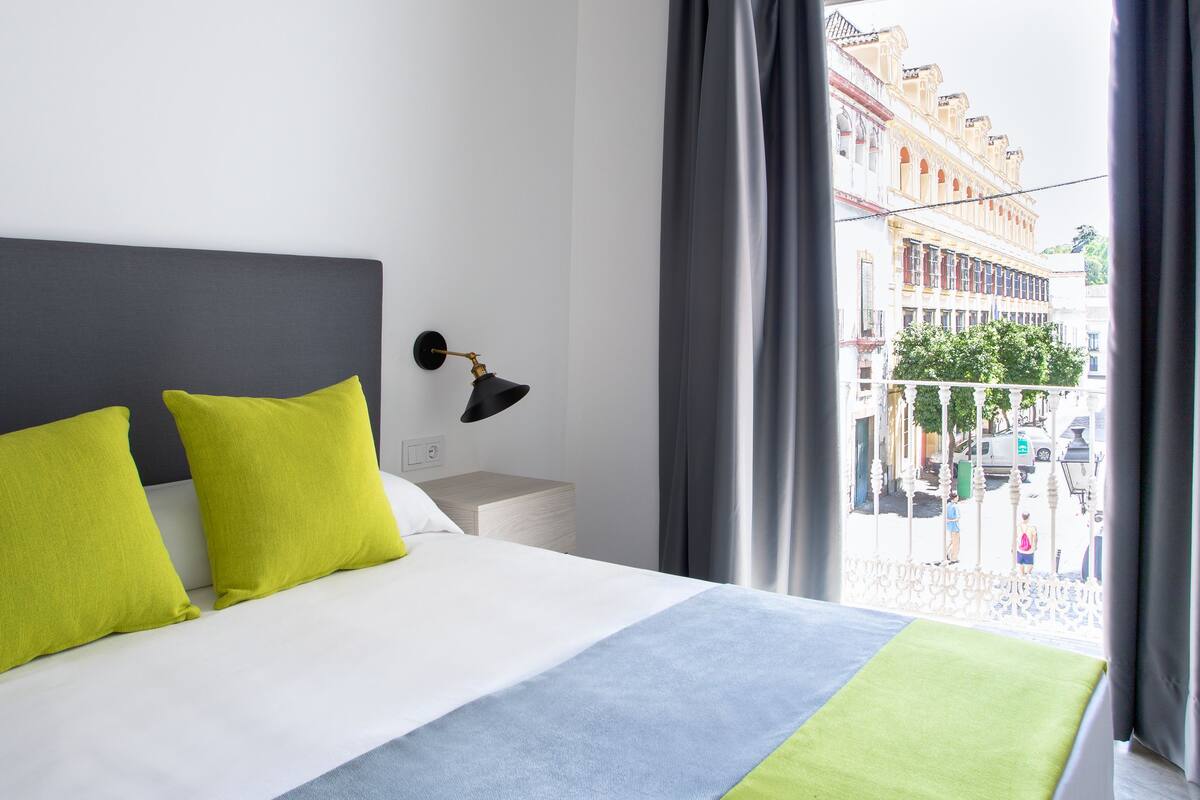 Een moderne hotelkamer met een groot bed, een nachtkastje, een lamp en uitzicht op de stad door een raam.