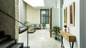 Un interno moderno con una scala, un soggiorno con divano e tavolino, e un corridoio con quadri appesi.