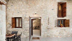 A stone-walled room with a wooden door, a staircase, and a small table with chairs. - Pagonas Traditional House (Apokoronas)