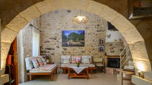 A stone-walled living room with a fireplace, a sofa, a coffee table, and a painting on the wall. - Pagonas Traditional House (Apokoronas)
