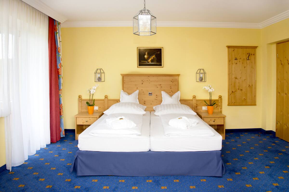 Una cama doble con sábanas blancas, dos mesitas de noche con lámparas, un cabecero de madera y una alfombra azul.