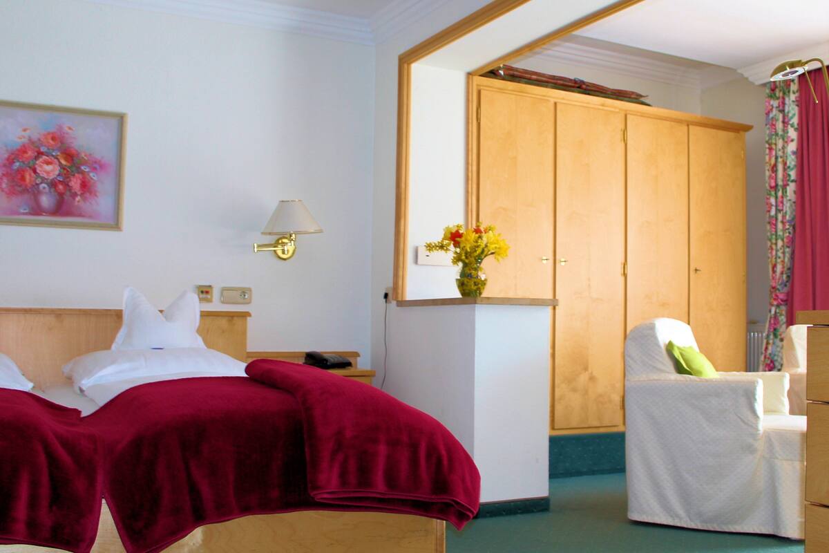 Una habitación de hotel con dos camas, un armario de madera, una silla, una lámpara y un cuadro en la pared.