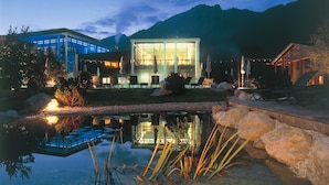 A modern building with a glass facade, a reflective pond, and a mountainous backdrop.