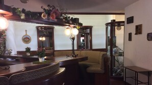 Eine gemütliche Bar mit einer gebogenen Holztheke, gepolsterten Sitzgelegenheiten und dekorativen Pflanzen.