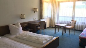 Ein Hotelzimmer mit zwei Einzelbetten, einem Schreibtisch, einem Stuhl und einem kleinen Tisch.