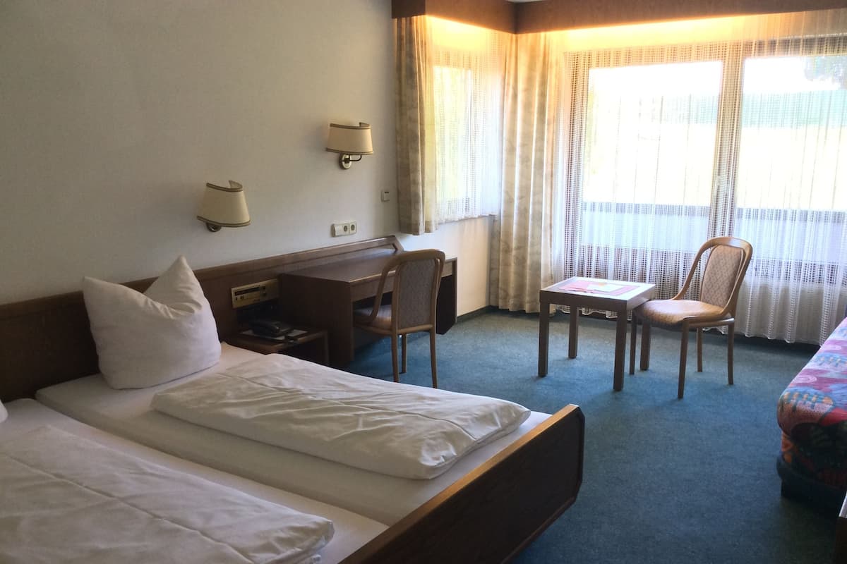 A hotel room with two single beds, a desk, a chair, and a small table.