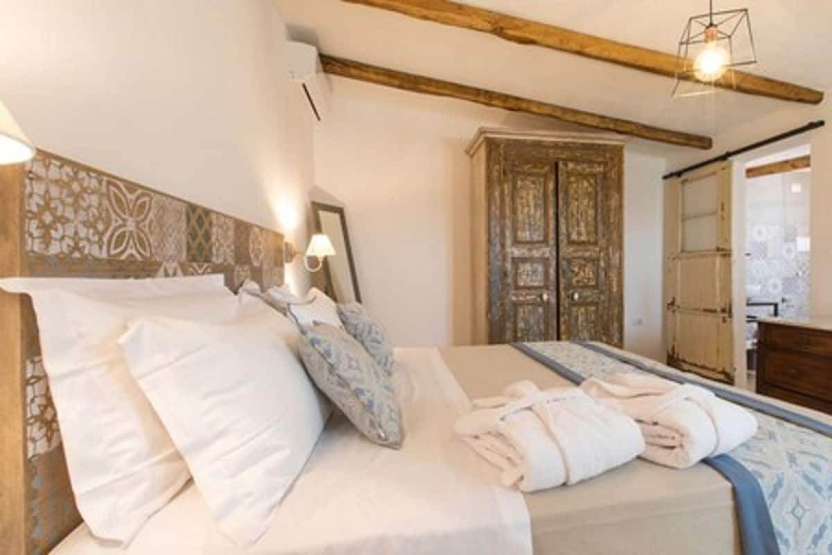 A neatly made bed with pillows and a blanket, a wooden headboard, a wall-mounted lamp, and a wooden wardrobe.