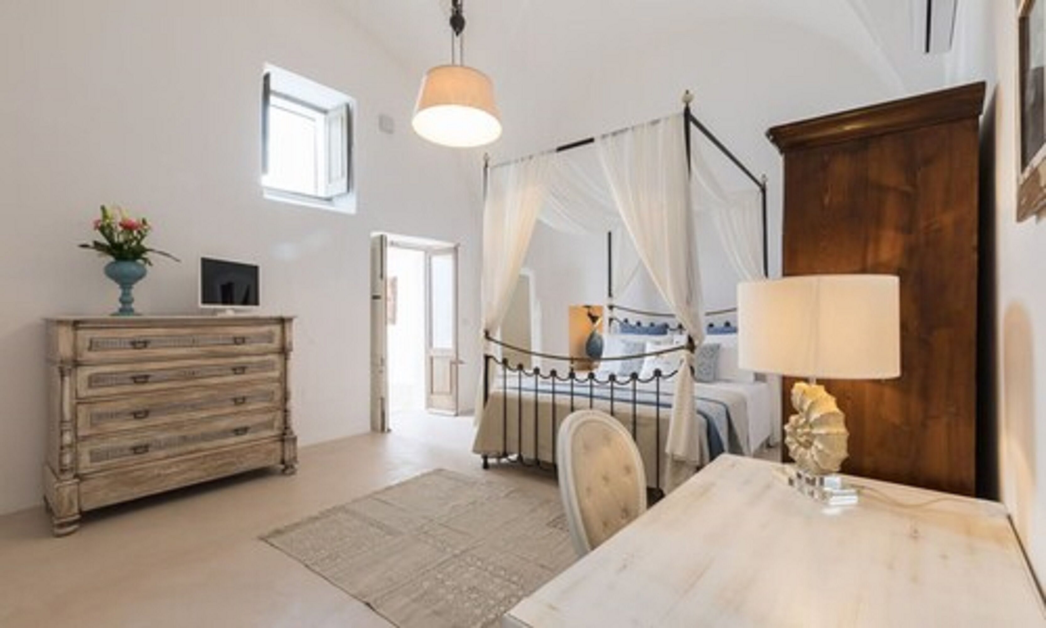 Une chambre à coucher avec un lit à baldaquin, une commode en bois, une table avec une lampe et une vue sur le couloir.