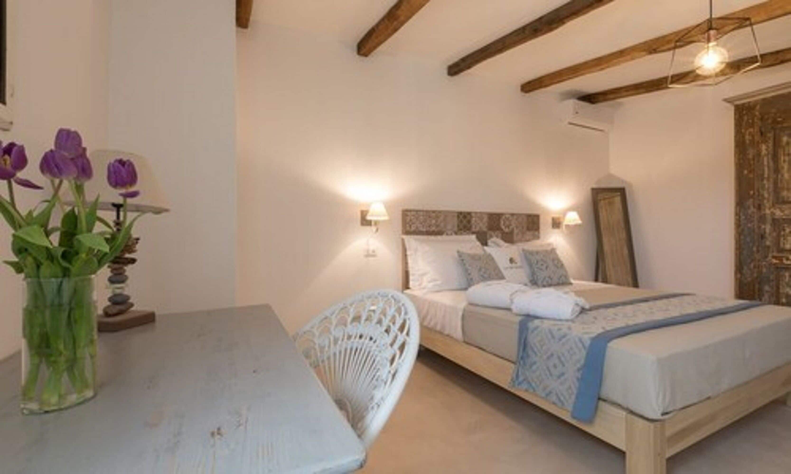 A bedroom with a bed, bedside lamps, a table with a vase of flowers, and a chair.