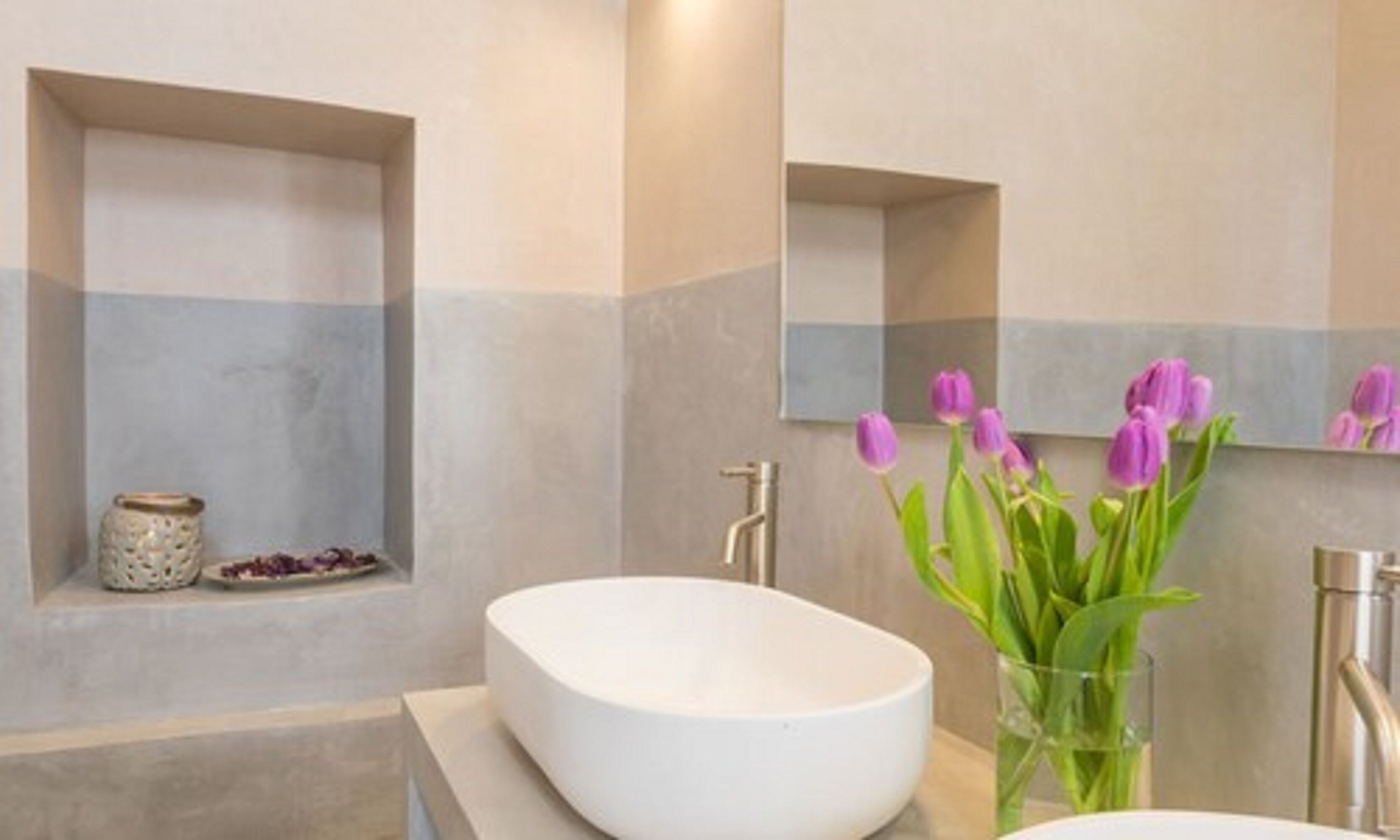 A bathroom with a large mirror, a white sink, and a vase with purple flowers.