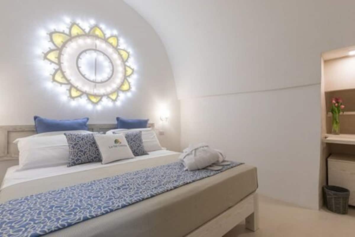 A modern hotel room with a bed, a wall-mounted light fixture, a small desk, and a trash bin.