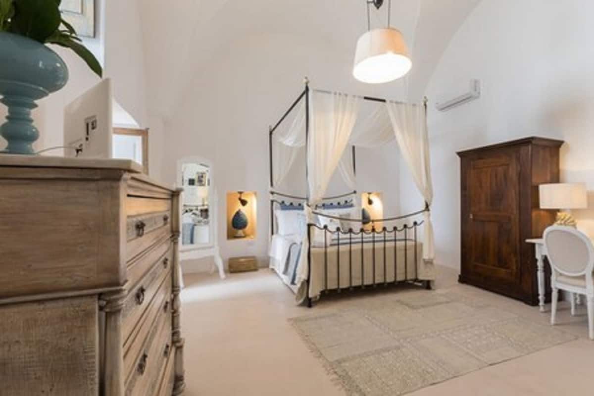 A bedroom with a four-poster bed, a wooden dresser, a desk with a chair, and a cabinet.