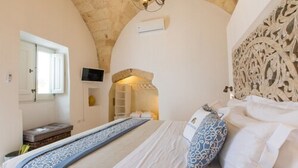 A bedroom with a bed, a television, and a stone wall. - Le Sei Conche Relais & Spa (Ugento)