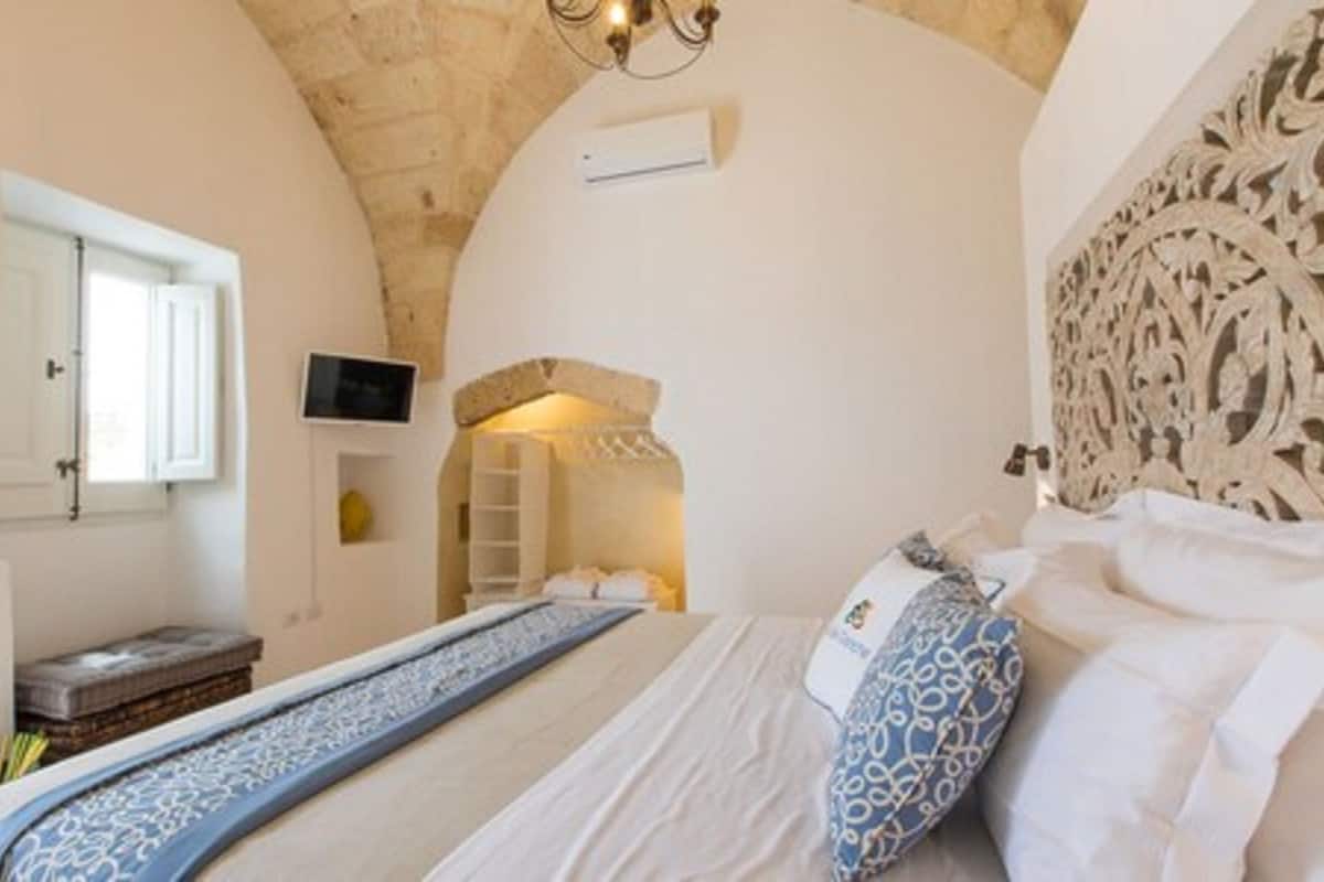 A bedroom with a bed, a television, and a stone wall.