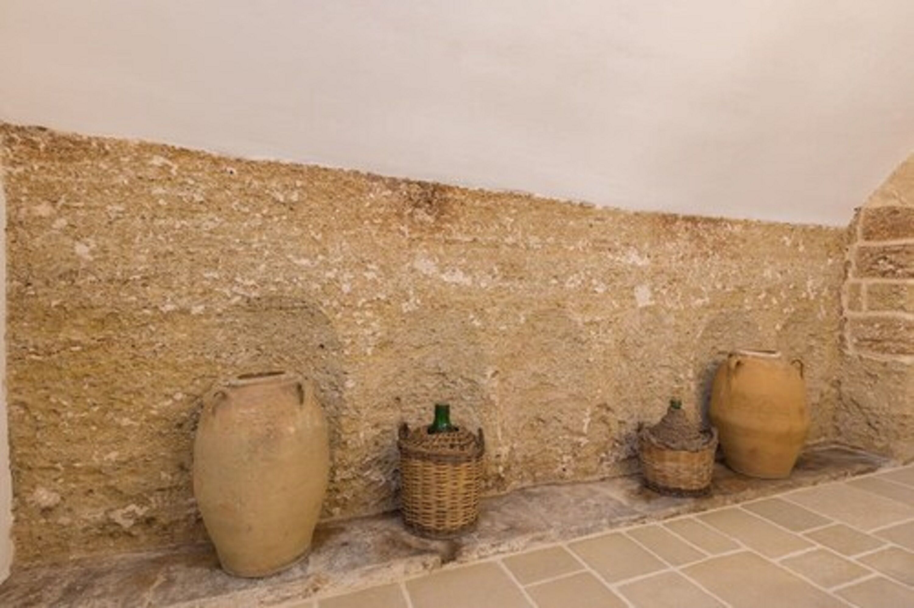 A rustic interior with a textured stone wall, a tiled floor, and three large ceramic pots of varying sizes.