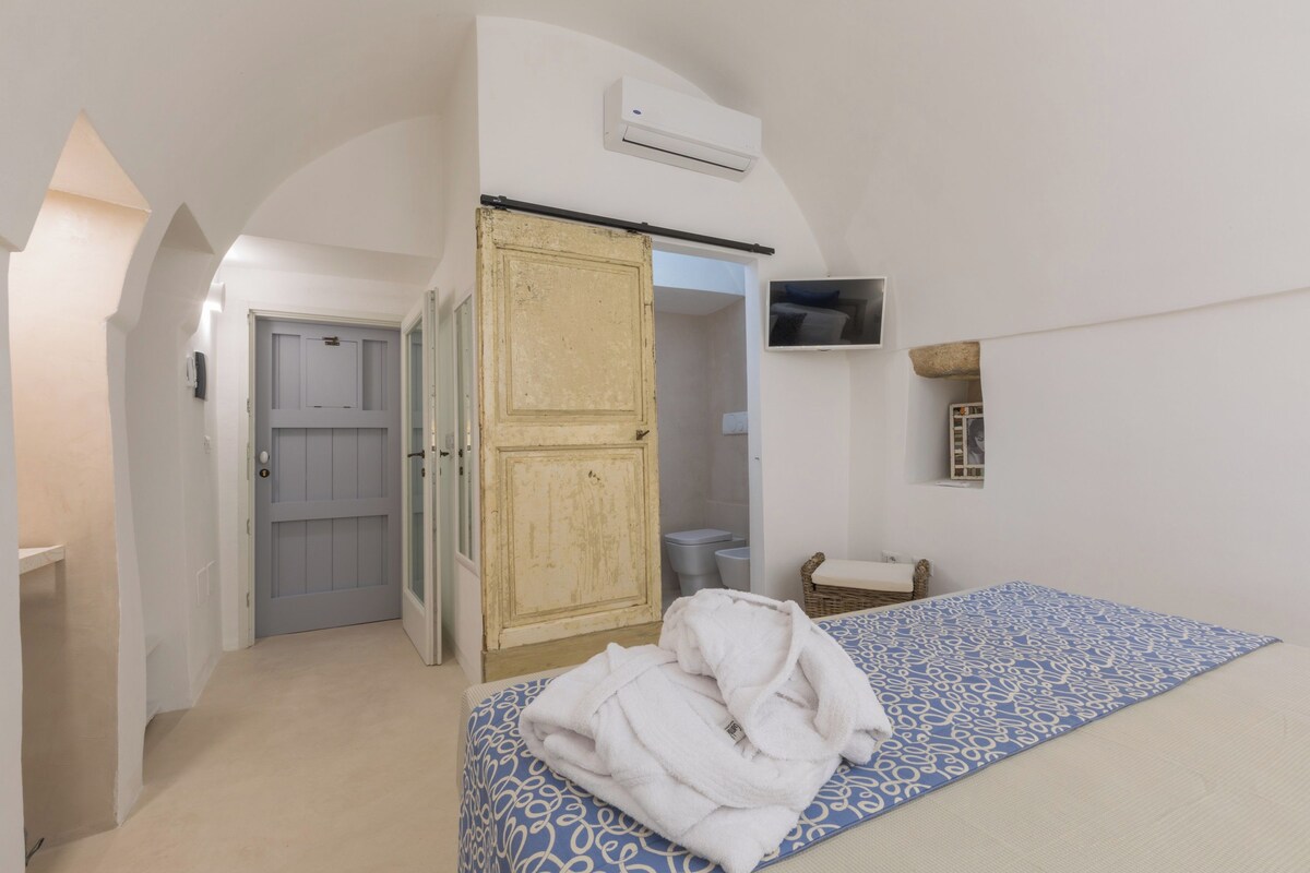 A bedroom with a bed, a wardrobe, a television, and a bathroom visible through an open door.