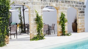 A poolside area with stone arches, outdoor seating, and greenery. - Le Sei Conche Relais & Spa (Ugento)