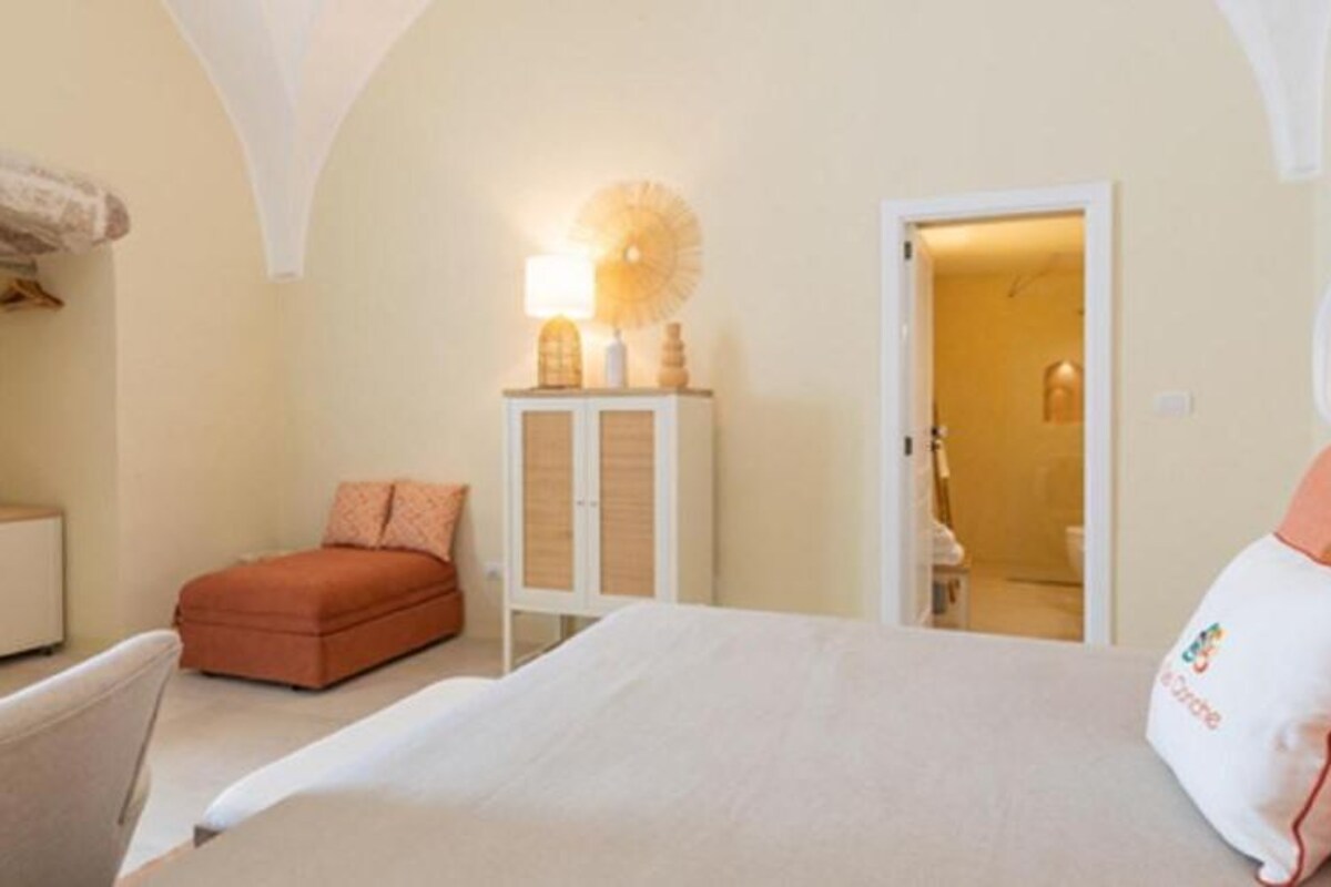 A bedroom with a bed, a chair, a cabinet, and a door leading to another room.