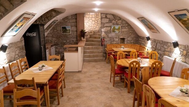 En restaurant med træborde og stole, stenvægge og en trappe, der fører op til en etage.