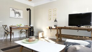 A living room with a wooden coffee table, a TV on a wooden stand, a fireplace, and a dining area with chairs and a table. - Gutshof Fürstenberg (Fürstenberg)
