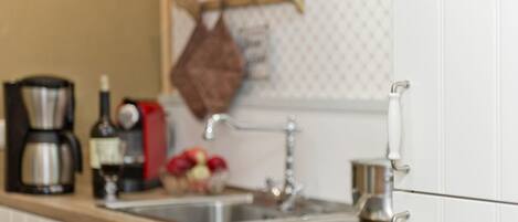 A kitchen with a wooden countertop, a coffee maker, a bottle, and a fruit bowl.