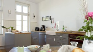 A modern kitchen with a central island, white cabinetry, and a large window. - Gutshof Fürstenberg (Fürstenberg)
