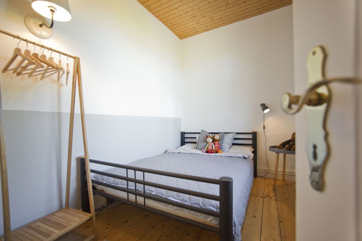 A bedroom with a wooden bed, a hanging clothes rack, a bedside lamp, and a small table.