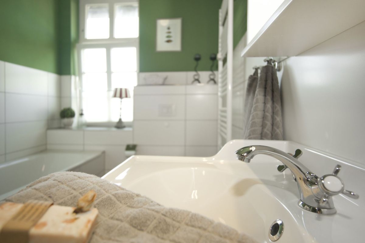 Un bagno con un lavandino bianco, pareti verdi e una finestra.