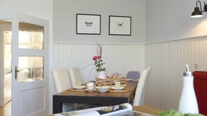 A dining area with a table set for two, a vase with flowers, and framed pictures on the wall. - Gutshof Fürstenberg (Fürstenberg)