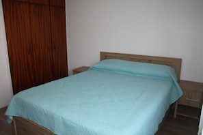 A single bed with a wooden headboard in a room with a wooden wardrobe and a nightstand. - By The Sea II (Limassol)