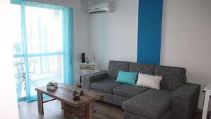 A living room with a grey sectional sofa, a wooden coffee table, and a white side table. - By The Sea II (Limassol)